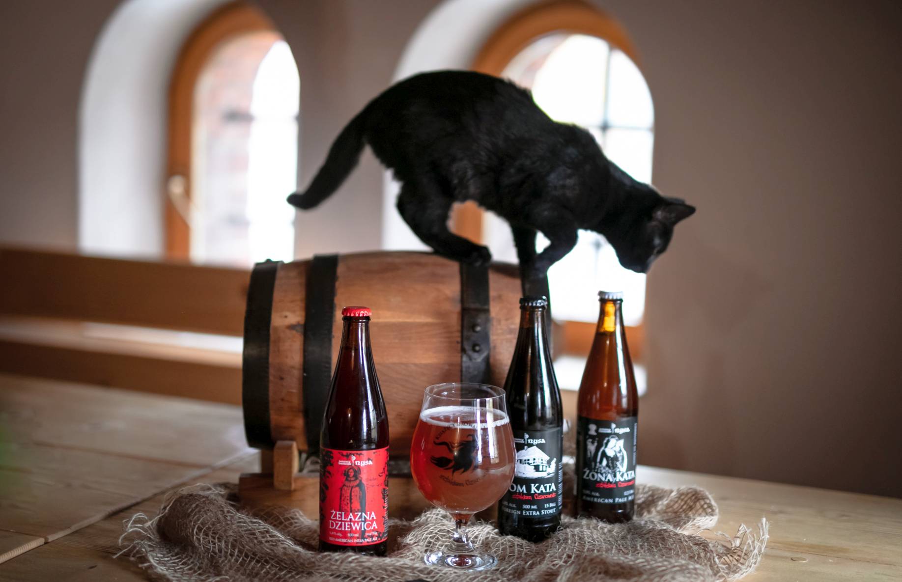 czarny kot zeskakujący z beczki z piwem, 3 piwa szlaku czarownic oraz jeden pełny kufel